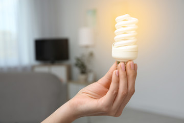 Woman holding lamp bulb in living room. Space for text