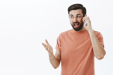 Excited man sharing awesome news via smartphone gesturing during talk looking away smiling...