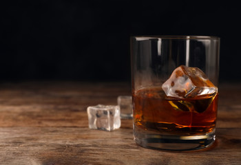 Golden whiskey in glass with ice cubes on table. Space for text