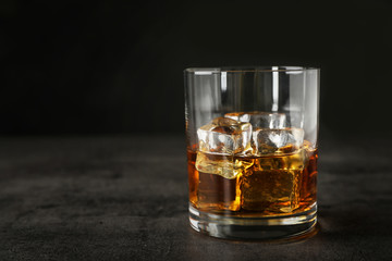 Golden whiskey in glass with ice cubes on table. Space for text