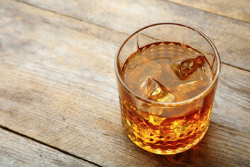 Golden whiskey in glass with ice cubes on table. Space for text