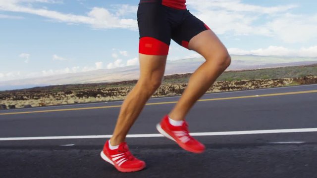 Triathlete running in triathlon suit training for ironman. Male runner exercising running uphill on road Big Island Hawaii. RED EPIC SLOW MOTION.