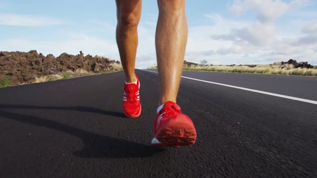Running shoes on male triathlete runner - close up of feet running on road. Man jogging outside exercising training for triathlon ironman. SLOW MOTION RED EPIC.