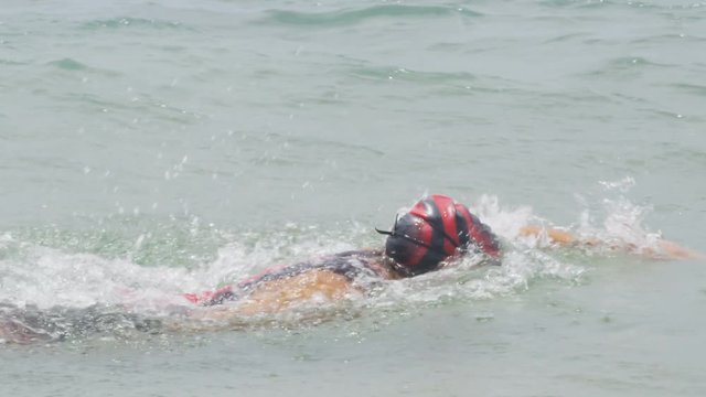 Triathlon man swimming - male triathlete swimmer in ocean doing freestyle crawl strokes. Fit man swimming in professional triathlon suit training for ironman on Hawaii. RED EPIC SLOW MOTION.