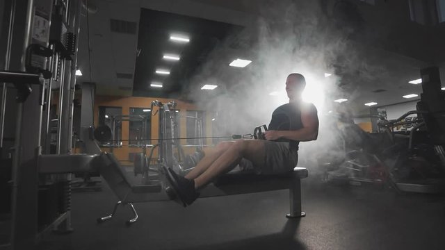 Man workout on fitness machine in dark gym. Very power athletic guy bodybuilder execute exercise with gym apparatus indoor.