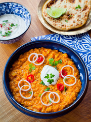 Indian Lentil Dal with red lentils, tomatoes, carrot, lime, cocnut cream, turmeric, curry powder, cumin seeds and mustard seeds. decorated with fresh cilantro, chilli and plant based coconut cream.