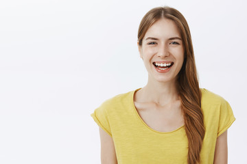 Close-up shot of kind happy charming european woman with braid in yellow birght t-shirt smiling joyfully at camera having fun enjoying nice friendly conversation standing against white background