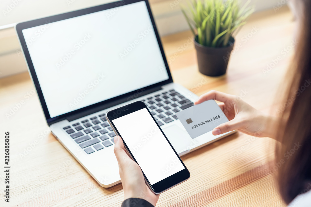 Aufkleber woman holding smartphone and using laptop on table in office room on windows with trees and nature b