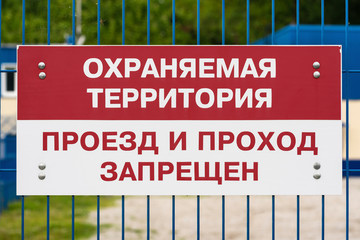Red and white prohibition sign on green lattice metal fence, text in Russian: Protected area,...