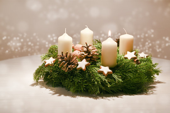 First Advent - decorated Advent wreath from fir and evergreen branches with white burning candles, tradition in the time before Christmas, warm background with festive bokeh and copy space