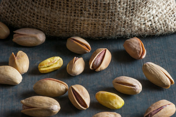 Obraz premium Pistachio in nutshell on black wooden rustic backdrop near burlap sack, composition of pistachios great for healthy and dietary nutrition. Concept of nuts