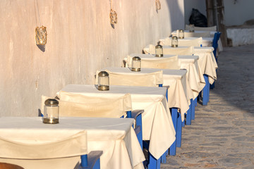 Perspective view of tables in a line outdoors in a Greek taverna in Hydra, Greece.