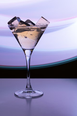 Cocktail glass with a drink and ice cubes in the neon light of a nightclub