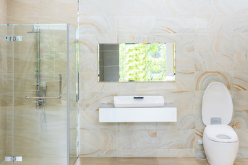 Bright new bathroom interior with glass walk in shower with white tile surround, toilet, bidet, basin and large mirror