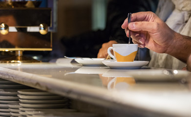 A male hand stirring an espresso coffee cup sitting in a bar counter in Italy, indoors.