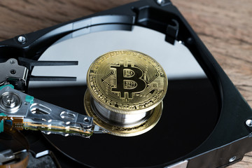 Bitcoin crypto currency digital money concept, shiny golden physical bitcoin coin with B sign on computer disk drive or hard drive data in low key on wooden table