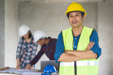 Portrait male engineer wearing safety helmet and holding blueprint in construction site.