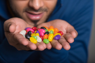 Man holding handful of jellybeans close to his face, handful of candy in focus