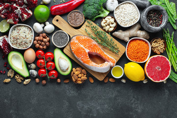 Healthy food clean eating selection: fish, fruit, nuts, vegetable, seeds, superfood, cereals, leaf vegetable on black concrete background with copy space. Flat lay