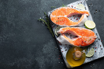 Two raw fresh salmon or trout steaks, rich in omega-3 oil, with lime, thyme and olive oil on a dark background. Healthy and dietary food. Top view with copy space. Flat lay