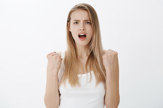 Studio shot of woman realising she lost being shocked and devestated as standing with clenched fists, hoping for victory looking desperate at camera with opened mouth from surprise and sadness