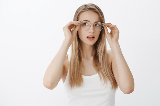 Girl sees better as trying new prescribed glasses ordered in shop. Portrait of intrigued charming calm and feminine young woman with blond hair putting on eyewear checking sight and lens dioptria