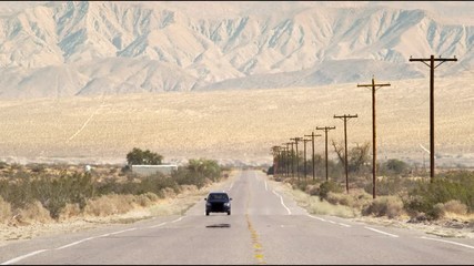 Car driving down hot desert road with mountain background