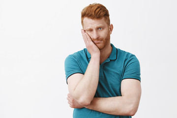 Man got stucked on parents meeting in school, feeling bored and uninterested. Gloomy indifferent redhead guy with bristle in green polo shirt, leaning face on palm and gazing aside with boredom