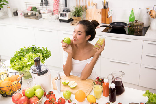 Asian woman in a kitchen with fruits and vegetables and juice
