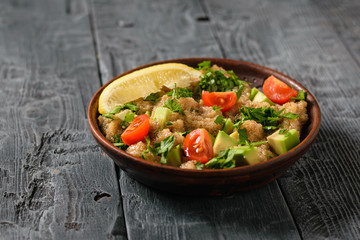 Salad of amaranth, avocado, pepper, lemon and parsley seeds with olive oil on a gray wooden table.