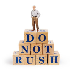 Adult caucasian man stands upon a heap of wooden blocks with a call Do Not Rush