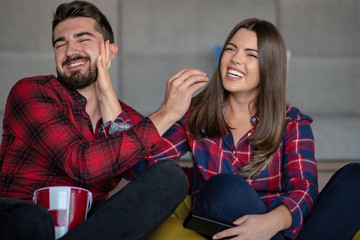 Couple fighting for remote control while watching TV at home
