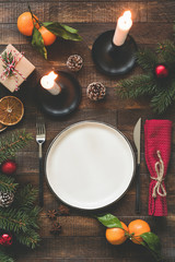 Rustic Christmas Table Setting With Candles, Empty Plate, Silverware, Pine Tree Branches, Cones And Tangerines. Top View