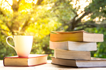 A cup of coffee and book on the wooden table and blurred nature background