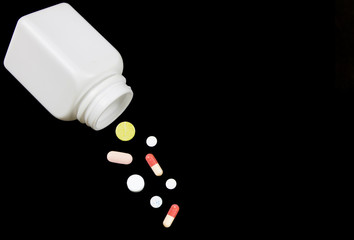 A white plastic bottle and pills with black background