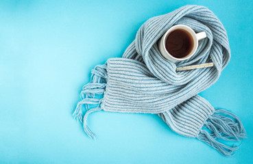 White mug of tea with blue scarf and thermometer on blue background. Disease and health concept.