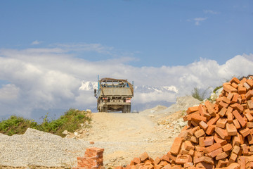 a pile of red bricks and a truck on a mountain road against the backdrop of snowy mountains and a blue sky
