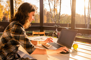 Young woman sitting on outdoor terrace and using laptop. Working mother has freelance job. Hands on computer keyboard. She looking at monitor. Home office, using mobile technologies, online shopping.