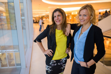 Two happy businesswomen inside shopping mall looking through window