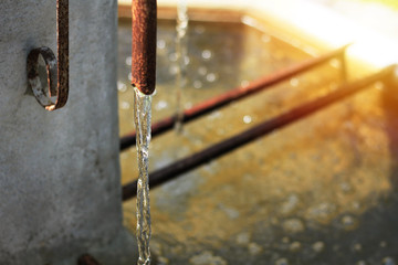 The water is flowing out of the rusty faucet. Into a pond made of cement - obrazy, fototapety, plakaty