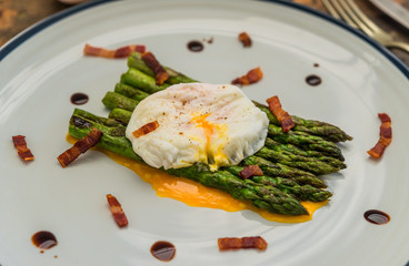 Food photography of a poached egg with asparagus, bacon, crispy bacon, and balsamic vinegar reduction. Breakfast, lunch, brunch, light dinner dish meal, healthy food, and clean eating concept.