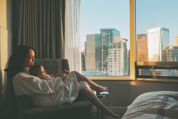 A mother holding her baby and relaxing in a hotel room. 