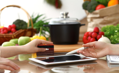 Close-up of human hands using tablet or touch pad. Two women in kitchen. Cooking, friendship or online shopping concepts