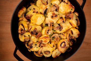 A photo of a pan with cooked vegetables, potatoes, green peas, mushrooms, shot from above on a dark rustic background, a vegan dinner
