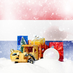 Christmas background.Toy truck with gifts, New Year fir, balls in the snowdrift and Netherlands flag