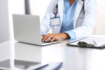 Fototapeta premium Unknown doctor woman typing on laptop computer while sitting at the desk in hospital office. close-up of hands. Physician at work. Medicine and health care concept