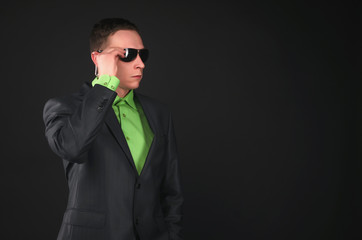 Fototapeta premium Security agent man in sunglasses and suit and with portable radio in his ear is intently looking forward isolated on black background.