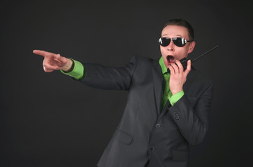 Scared security agent is talking on the portable radio station and is showing ahead by his index finger isolated on black background.
