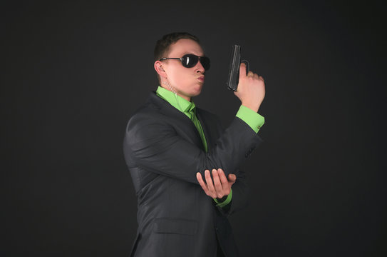 Arrogant security agent is posing with a gun in hand like a super spy isolated on black background.