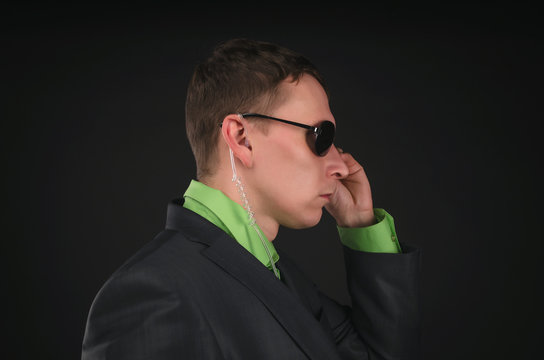 Security agent man in suit and sunglasses with portable radio in the ear isolated on black background.